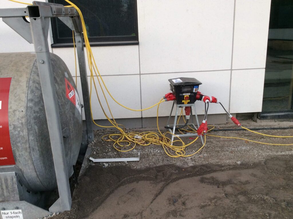 Elektrische verdeelkast met gele kabels naast een brandstoftank op de ziekenhuiswerf