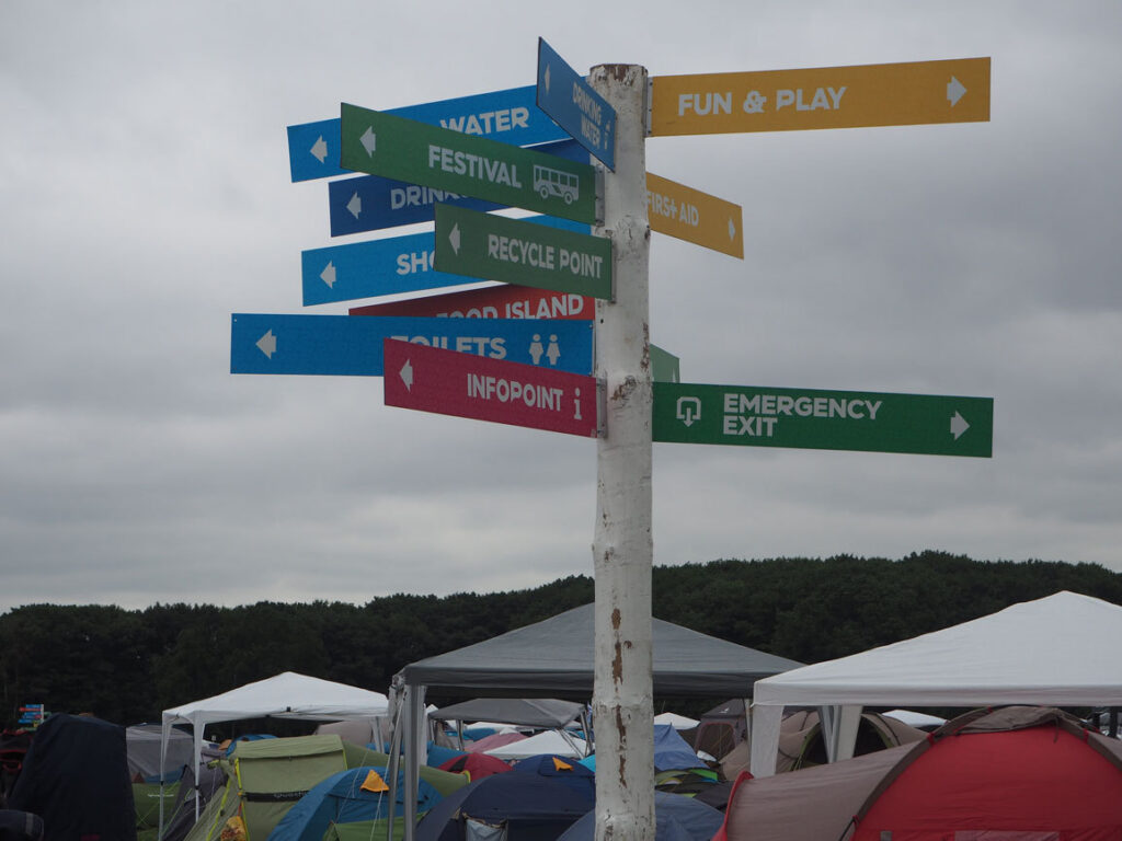 Kleurrijke wegwijzer naar infopoint en nooduitgang boven de festivalcamping van Pukkelpop