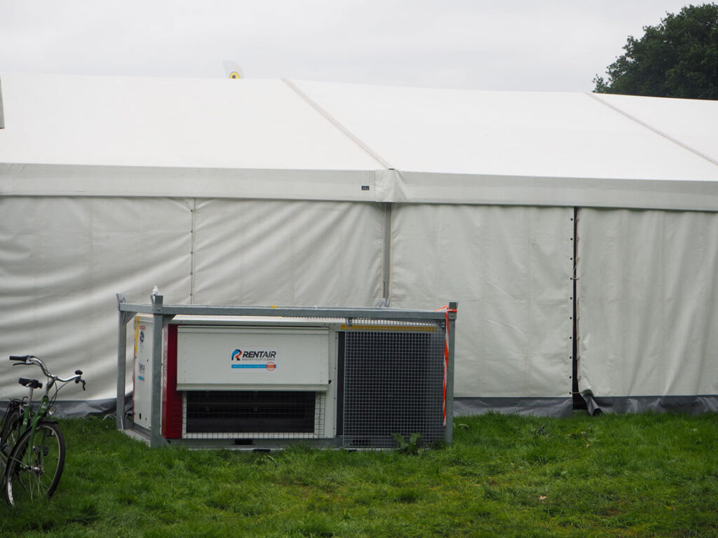 Mobiele airco-unit van Rentair op het gras voor een witte tent, met een fiets ernaast