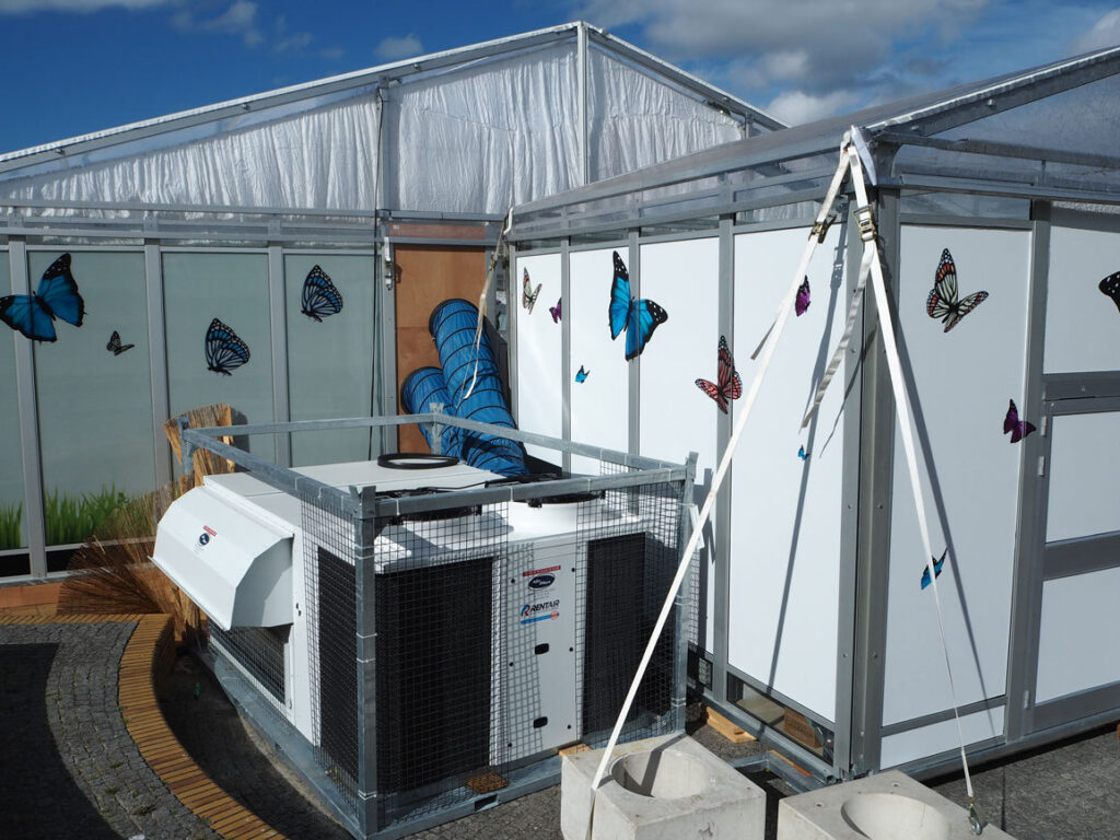 Rooftop airco-unit met blauwe luchtslang naast de pop-up vlindertuin in Knokke