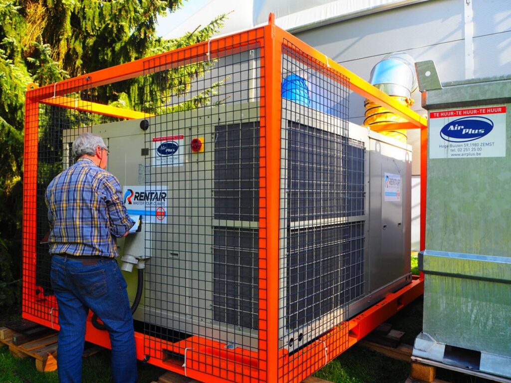 Man bij de rooftop airco van 70 kW in een oranje gaaskooi in Houffalize