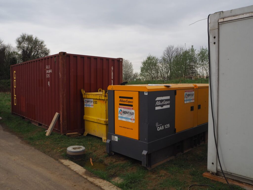 Generator van 125 kVA en ADR-olietank naast een rode container op de werf in Vorst