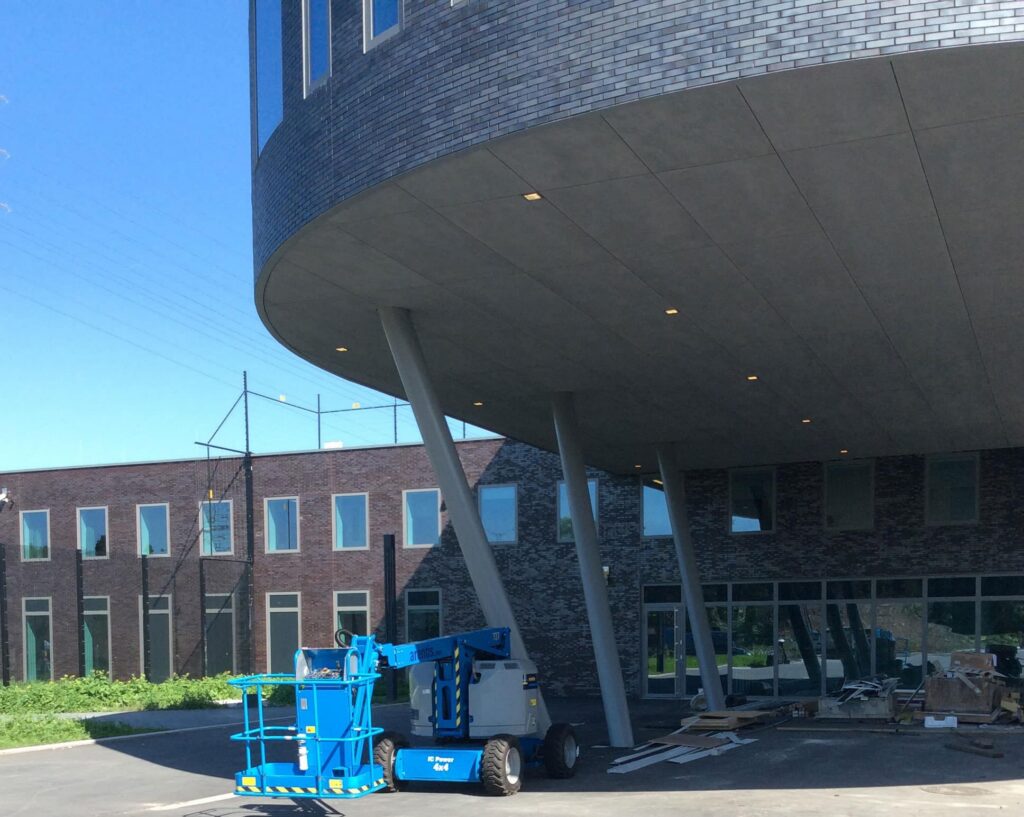 Nieuwbouw van het forensisch psychiatrisch centrum in Gent met een blauwe hoogwerker onder de overkapping